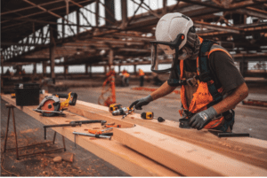 A person in an orange vest and hard hat working on wood.